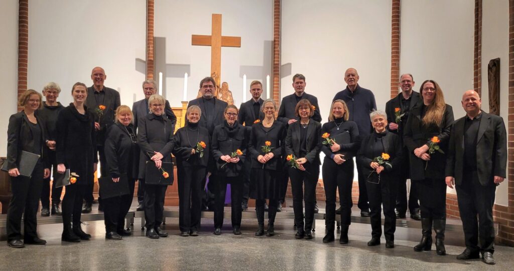 Der Wandsbeker Kammerchor steht nach einem Auftritt in schwarzer Chorkleidung mit Rosen in der Hand im Altarraum einer Kirche.